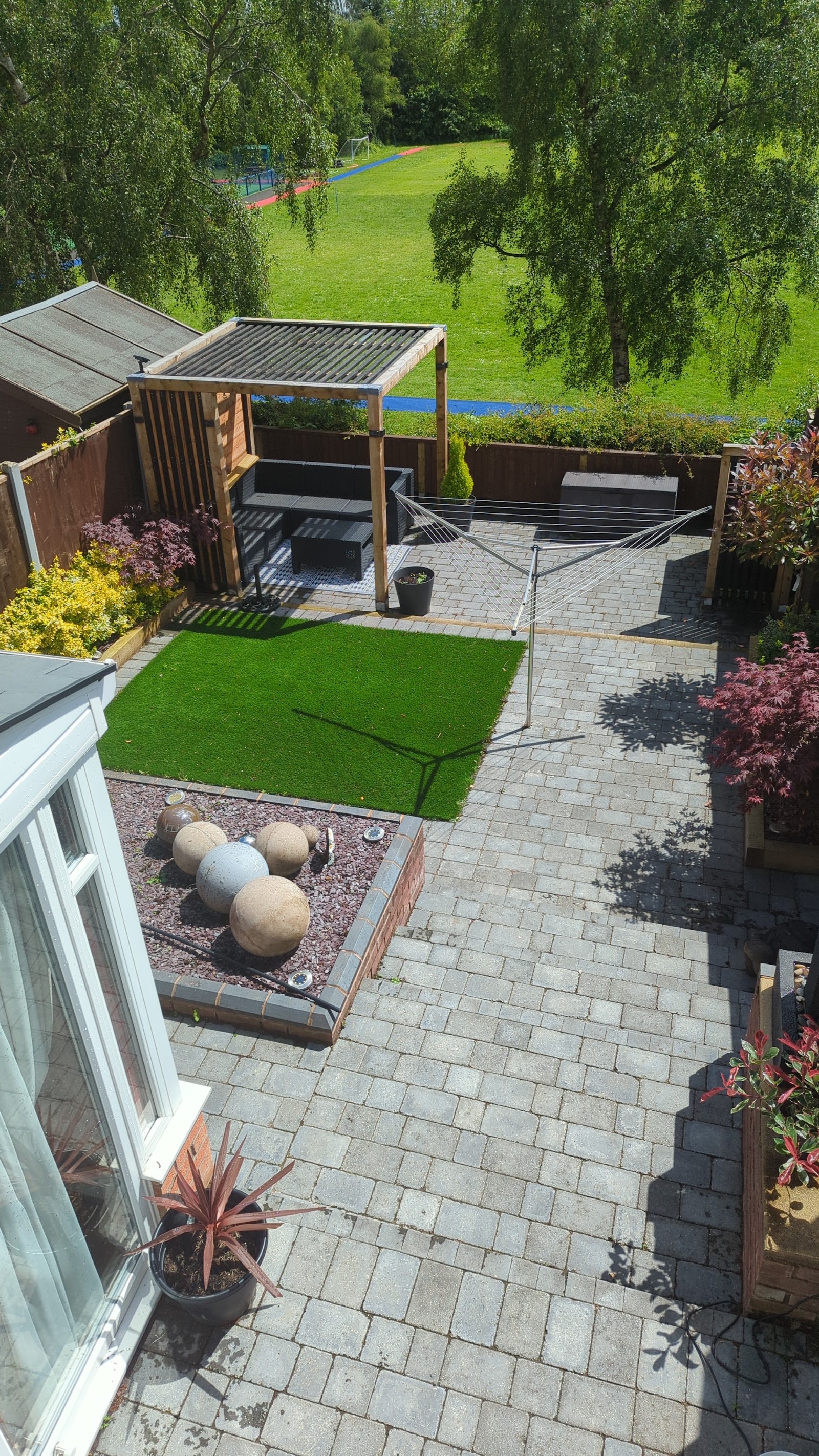 Block-paved patio with pergola, artificial lawn and stone spheres in a landscaped Walsall garden